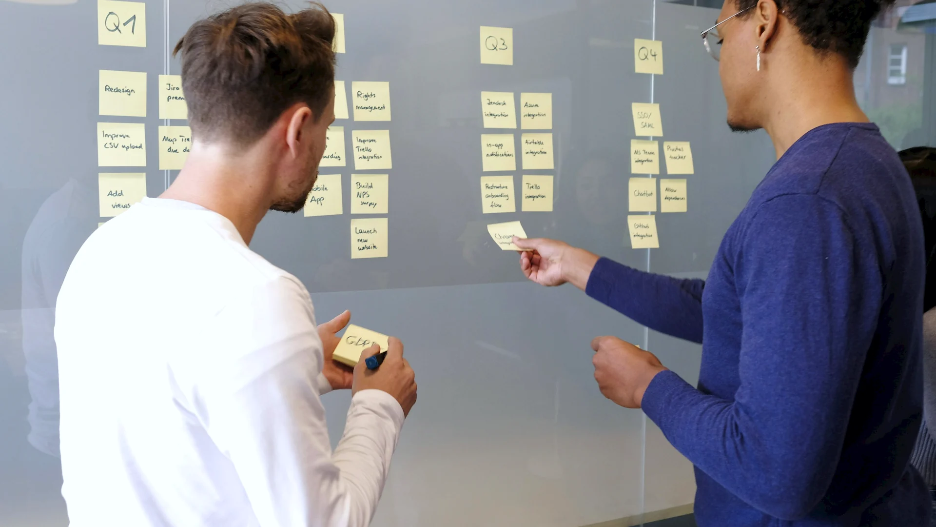 Zwei Personen planen ein Projekt mit Haftnotizen an einer Glaswand